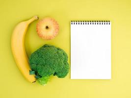 frutas y verduras - manzana, plátano y brócoli sobre fondo amarillo brillante. cuaderno para registrar sobre nutrición adecuada, vitaminas, estilo de vida saludable.
