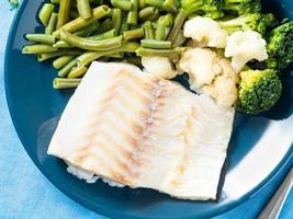 Steamed seafood cod fillet with vegetables on a blue plate, top view, close up. Healthy diet food for proper nutrition