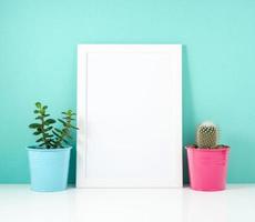 marco blanco en blanco, plantar cactus en una mesa blanca contra la pared azul. maqueta con espacio de copia. foto