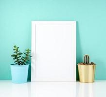 Blank white frame, plant cactus on white table against the blue photo