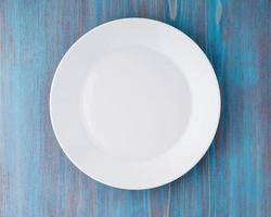 big flat empty white plate on a blue wooden table, top view photo