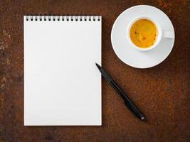 hoja en blanco vacía de cuaderno con espiral, lápiz y taza de café sobre una mesa de hierro oxidada, vista superior. foto