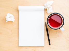 Open notebook with a white clean sheet for notes and drawing, wrinkled paper, pencil and mug of tea. Light wood background, top view. photo