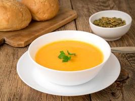 white bowl of pumpkin soup, garnished with parsley on wooden background, side view. photo