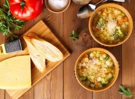 Two bowl of minestrone soup with cheese on cutting board and vegetables photo