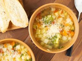 Two bowl of minestrone soup with toast on rustic wooden background, top view, close up photo