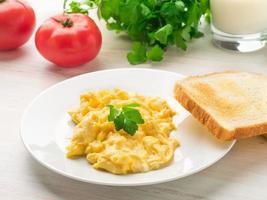 white plate with pan-fried scrambled eggs on a white light background with tomatoes. Omelette, side view photo