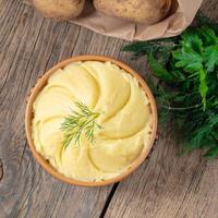 Mashed potatoes, boiled puree in brown bowl on dark wooden rustic background, top view photo