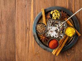 Oriental spice set - coriander, red pepper, turmeric, cinnamon, star anise, various seasonings in metall cups, on brown dark wooden table, top view, macro, empty space. photo