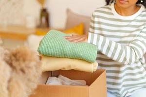 Faceless ethnic female putting clothes in box. Concept of moving house and packing stuff photo