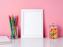 marco blanco en blanco y crayón en frasco, caramelos en una mesa blanca contra la pared rosa con espacio para copiar foto