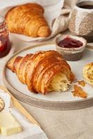 Two delicious croissants on plate and hot drink in mug, side view, vertical photo