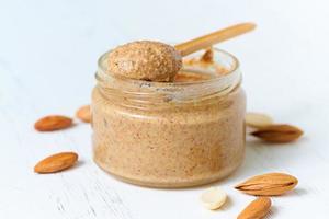 nut butter, crunchy and stir, white wooden table, glass jar, side view, close up photo