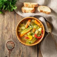 Bright spring vegetable dietary vegetarian soup. Top view, brown rustic wood background, linen napkin. photo