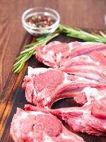 Raw lamb cutlets on bone on dark brown wooden background, lamb ribs, side view, vertical photo
