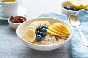 Whole oatmeal, large bowl of porridge with banana, blueberries, apple, nuts. Side view, close up photo