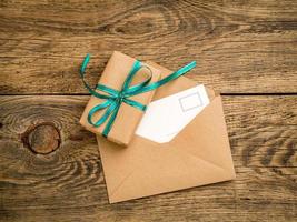 holiday gift box, tied with green ribbon, open envelope of Kraft paper with postcard, letter on the wooden weathered rustic background, top view. photo