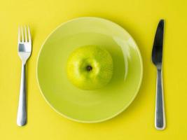 green ripe apples on a bright green plate, knife, fork on colorful yellow and green background, top view photo