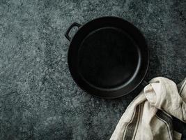 blank cast iron frying pan on dark grey concrete background, top view, blank space for text photo