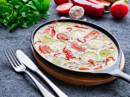 Pan with traditional Italian Frittata on dark gray stone table, forks, parsley, pepper, tomatoes. Scrambled eggs photo