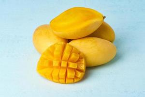 Four whole mango fruits on bright blue table and cut into slices. Large juicy yellow fruits photo