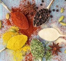 Milled spices - garlic, turmeric, paprika, anise, oregano, cardamom. Round of golden spoons on blue wooden table. Top view, close-up photo