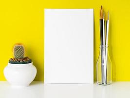 Mockup with clean white canvas, cactus, brushes on bright yellow background. Concept for creativity, drawing. photo