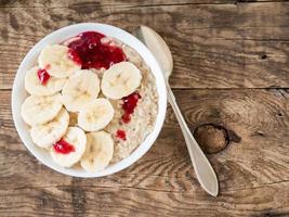 Healthy Breakfast in the morning - oatmeal with slices of bananas and raspberry jam. Top view. photo