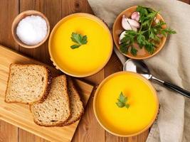 Two brown bowl of pumpkin soup with parsley on brown dark wooden background, top view photo