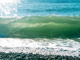 Sea wave with foam, beach, pebble, sun glare on the water, black sea coast. Horizontal framing. photo