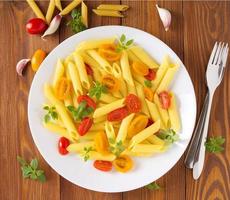 pasta penne con tomates amarillos y rojos decorados con albahaca sobre fondo de madera marrón foto