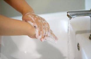 Hygiene. Cleaning Hands. Washing hands with soap. Young woman washing hands with soap over sink in bathroom, closeup. Covid19. Coronavirus. photo