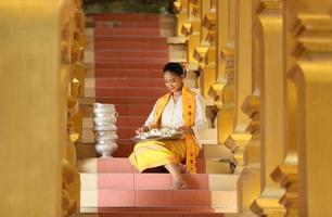 Young Asian girl in traditional Burmese costume holding bowl of rice on hand at golden pagoda in Myanmar temple. Myanmar women holding flowers with Burmese traditional dress visiting a Buddhist temple photo