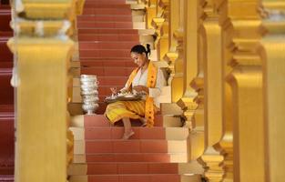 Young Asian girl in traditional Burmese costume holding bowl of rice on hand at golden pagoda in Myanmar temple. Myanmar women holding flowers with Burmese traditional dress visiting a Buddhist temple photo