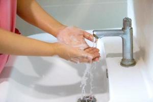 Hygiene. Cleaning Hands. Washing hands with soap. Young woman washing hands with soap over sink in bathroom, closeup. Covid19. Coronavirus. photo