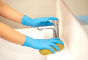 Person, a hand in a blue rubber glove in the picture, removes and washes bathroom sink photo