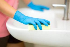 persona, una mano en un guante de goma azul en la foto, quita y lava el lavabo del baño