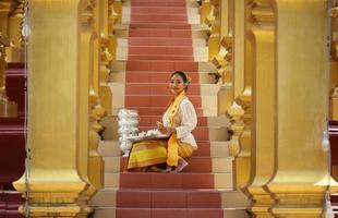 Young Asian girl in traditional Burmese costume holding bowl of rice on hand at golden pagoda in Myanmar temple. Myanmar women holding flowers with Burmese traditional dress visiting a Buddhist temple