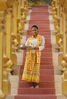 Young Asian girl in traditional Burmese costume holding bowl of rice on hand at golden pagoda in Myanmar temple. Myanmar women holding flowers with Burmese traditional dress visiting a Buddhist temple