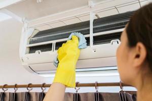 Asian woman cleaning a dirty and dusty air conditioning filter in her house. Housewife removing a dusty air conditioner filter. photo