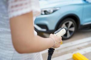 mujer hermosa joven asiática preparándose para cargar un vehículo eléctrico o ev en la estación de carga ev. foto