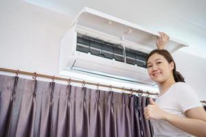 mujer asiática limpiando un filtro de aire acondicionado sucio y polvoriento en su casa. ama de casa quitando un filtro de aire acondicionado polvoriento. foto