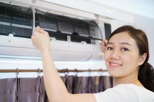 mujer asiática limpiando un filtro de aire acondicionado sucio y polvoriento en su casa. ama de casa quitando un filtro de aire acondicionado polvoriento. foto