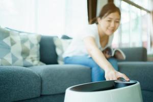 Asian young beautiful woman turning on the air purifier machine during living in the living room. photo