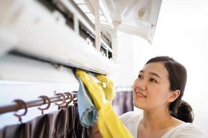 mujer asiática limpiando un filtro de aire acondicionado sucio y polvoriento en su casa. ama de casa quitando un filtro de aire acondicionado polvoriento. foto