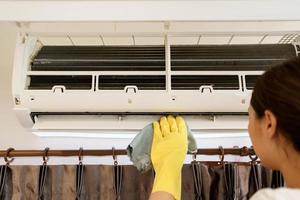 Asian woman cleaning a dirty and dusty air conditioning filter in her house. Housewife removing a dusty air conditioner filter. photo