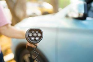 mujer irreconocible preparando un conector de carga ev para cargar un vehículo eléctrico. foto