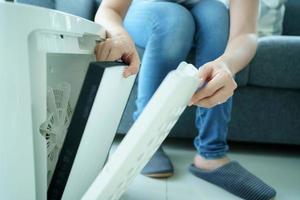 hermosa joven asiática sosteniendo un filtro purificador de aire de carbono hepa en la sala de estar, la mujer prepara un filtro purificador de aire para reemplazar el anterior. concepto de salud y buen estilo de vida. foto