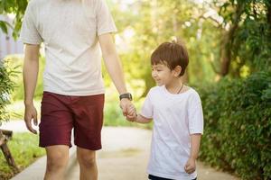 un niño asiático feliz disfruta jugando y caminando en el parque con papá cerca, un niño asiático tiene una hermosa sonrisa mientras mira a su padre. retrato de niño pequeño en el parque y el patio de recreo. foto