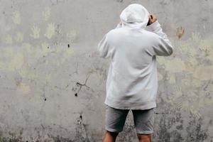 maqueta de sudadera con capucha de vista posterior de un hombre de pie frente a la pared foto